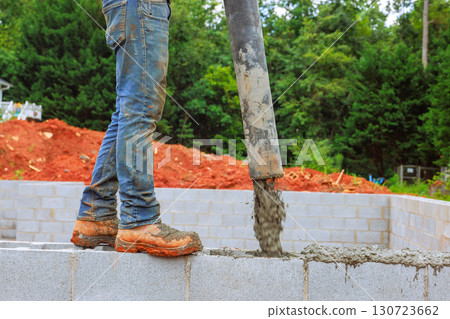 Contractor worker directs concrete from chute into foundation blocks on work day 130723662