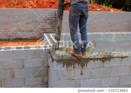 Construction worker pours cement to create sturdy walls at building site during works day. Construction worker pours cement to create sturdy walls at building site during works day. 130723663