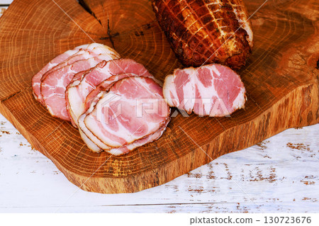 Cured meat is beautifully sliced on wooden board, adding rustic charm to kitchen atmosphere. 130723676