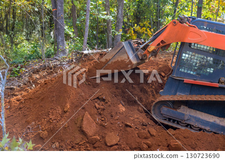 Heavy machinery digs into soil, clearing ground for construction in wooded location. Heavy machinery digs into soil, clearing ground for construction in wooded location. 130723690