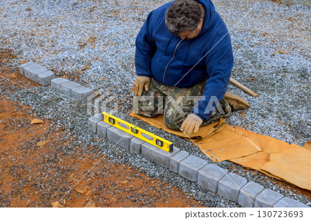 Worker is carefully lining up gray bricks using level tool at construction site. Worker is carefully lining up gray bricks using level tool at construction site. 130723693