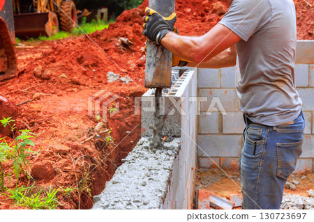 Worker uses concrete pump to pour cement into block wall being constructed outdoors in works day Worker uses concrete pump to pour cement into block wall being constructed outdoors in works day 130723697