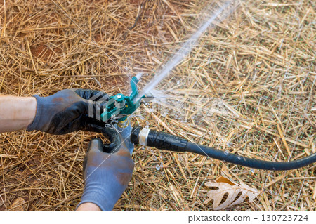 Person is repairing garden sprinkler system on warm afternoon among dry grass garden tools scattered nearby. Person is repairing garden sprinkler system on warm afternoon among dry grass garden tools scattered nearby. 130723724