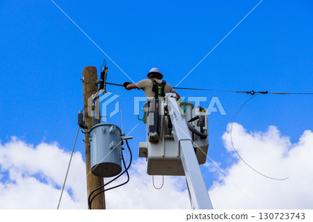 Electrical utility worker uses cherry picker to repair electrical lines on pole under work maintenance day 130723743