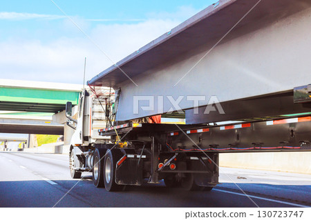 Heavy truck carries sizable concrete beam on highway under driving day passing beneath an overpass structure. Heavy truck carries sizable concrete beam on highway under driving day passing beneath an overpass structure. 130723747