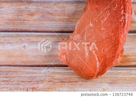 Fresh cut of raw steak rests on rustic wooden surface, ready for seasoning cooking. 130723748