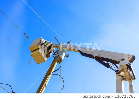 Utility workers are repairing electrical lines from cherry picker under bright blue sky. Utility workers are repairing electrical lines from cherry picker under bright blue sky. 130723765