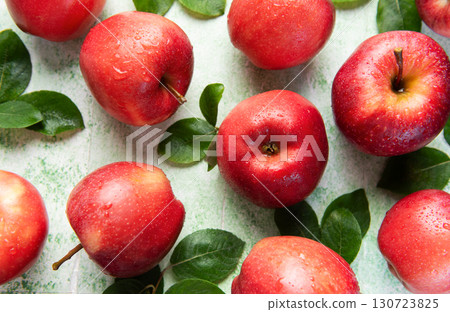 Fresh red apples with green leaves creating appealing pattern on green background 130723825