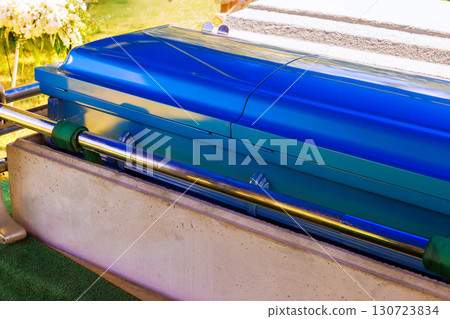 Bright blue casket is placed on gurney surrounded by greenery at memorial service in peaceful cemetery Bright blue casket is placed on gurney surrounded by greenery at memorial service in peaceful cemetery 130723834