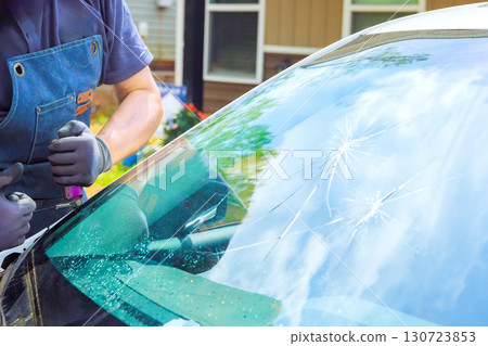 Technician works on damaged windshield from vehicle parked in suburban driveway on replace windshield Technician works on damaged windshield from vehicle parked in suburban driveway on replace windshield 130723853