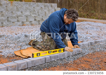 Worker carefully aligns stones while building pathway on gravel surface during work day Worker carefully aligns stones while building pathway on gravel surface during work day 130723856