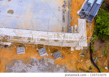 Scaffolding encircles partially built structure, with construction materials scattered around, active work day 130723870
