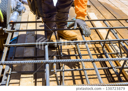 Construction worker assembling metal rebar grid framework for building, under construction work day 130723879