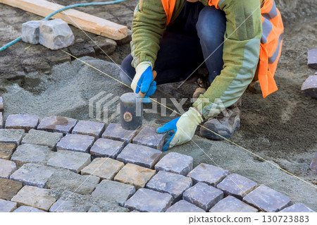 Worker uses mallet to carefully place cobblestones for perfect, aligned fit. 130723883