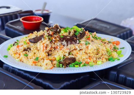 Delicious beef fried rice with vibrant vegetables green onions arranged on platter at an outdoor event. Delicious beef fried rice with vibrant vegetables green onions arranged on platter at an outdoor event. 130723929