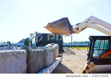 Heavy machinery is in operation, transferring large concrete blocks onto waiting truck under works day. 130723956