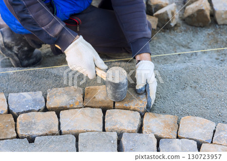 Worker carefully places stones while building pathway in residential yard under work day Worker carefully places stones while building pathway in residential yard under work day 130723957