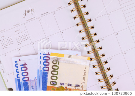 July's calendar with South Korean won banknotes placed beside it, illustrating budget planning for month. 130723960