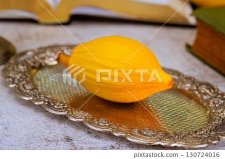 During Hebrew tradition yellow etrog rests on an ornate silver platter, surrounded by aged books, Jewish holiday Sukkot festival During Hebrew tradition yellow etrog rests on an ornate silver platter, surrounded by aged books, Jewish holiday Sukkot festival 130724016