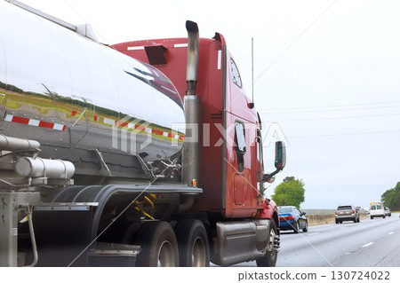 Red truck with reflective fuel tank travels down busy highway on American cloudy day. Red truck with reflective fuel tank travels down busy highway on American cloudy day. 130724022