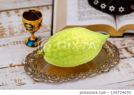 Jewish festival of Sukkot with citron etrog rests on silver tray next to decorative cup open Jew Holy book Jewish festival of Sukkot with citron etrog rests on silver tray next to decorative cup open Jew Holy book 130724030