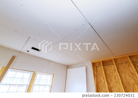 Drywall being installed in residential room, with visible seams natural light coming through windows. 130724031