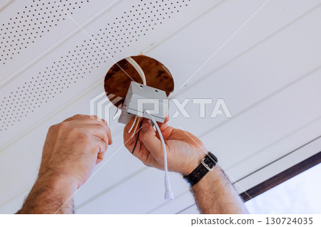 Electrical worker connects wires to junction box mounted in ceiling of renovated living space. 130724035