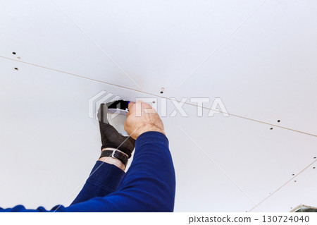 Professional works on repairing hole in drywall ceiling of home, demonstrating careful craftsmanship. 130724040