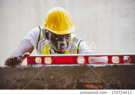 Black engineer checking wall alignment with spirit level at construction site 130724412