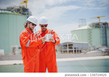 Oil and gas engineers in protective gear discussing LNG project at coastal storage facility Oil and gas engineers in protective gear discussing LNG project at coastal storage facility 130724420