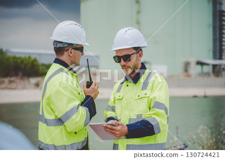 Two engineers using radio and tablet at coastal oil gas facility in safety jackets Two engineers using radio and tablet at coastal oil gas facility in safety jackets 130724421