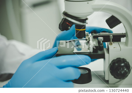 Professional scientist analyzing sample through microscope in modern research laboratory setting 130724440