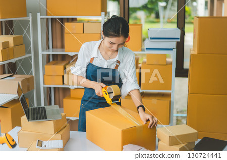 Startup small business owners holding packing machine and sealing cardboard boxes with tape to deliver products to customers- concept shopping online Startup small business owners holding packing machine and sealing cardboard boxes with tape to deliver products to customers- concept shopping online 130724441