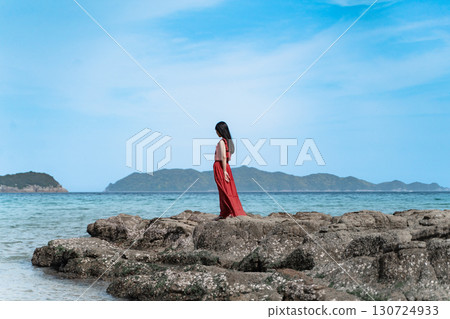 A woman in a red dress standing on the beach① 130724933
