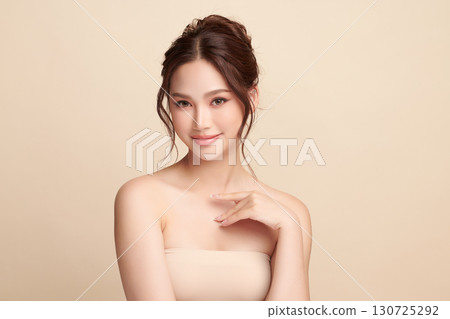 A beautiful young Asian woman with clean, fresh skin against a beige background. Skincare, facial treatment, cosmetology, beauty, and spa. An elegant portrait of an Asian woman. 130725292