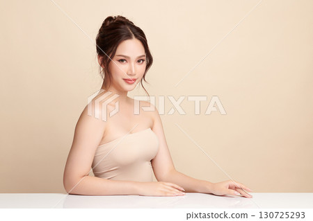 A beautiful young Asian woman with clean, fresh skin against a beige background. Skincare, facial treatment, cosmetology, beauty, and spa. An elegant portrait of an Asian woman. 130725293
