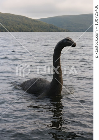 A mysterious aquatic creature resembling the Loch Ness Monster emerges from the surface of a lake in a natural landscape 130725436