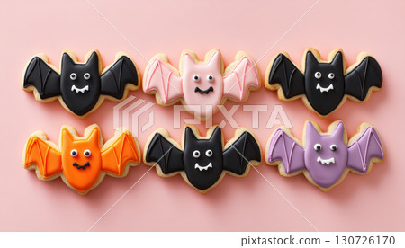 Smiling bat shaped cookies with colorful icing, including black, pink, orange, and purple, arranged on pastel background, creating playful and festive mood 130726170