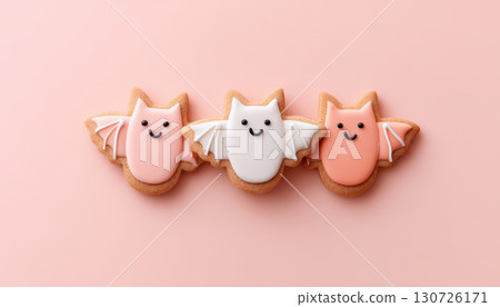 Smiling bat shaped cookies with colorful icing, cute faces, pastel colors, and playful design on pink background, perfect for Halloween or party decoration 130726171