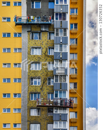Workers perform building maintenance on a colorful high-rise in a sunny urban environment 130726352