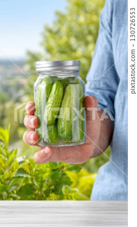 A person holds a glowing jar filled with pickles in a vibrant garden on national pickle day A person holds a glowing jar filled with pickles in a vibrant garden on national pickle day 130726553