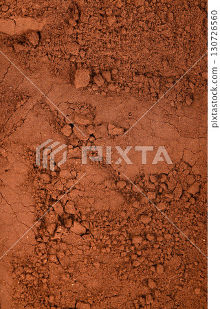 A detailed close-up texture of dark red and brown soil, illustrating a dry and cracked surface. A detailed close-up texture of dark red and brown soil, illustrating a dry and cracked surface. 130726560