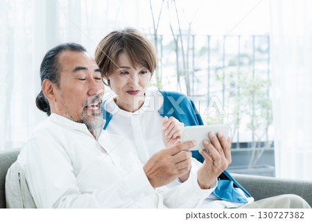 坐在沙發上看智慧型手機的老年夫婦 130727382