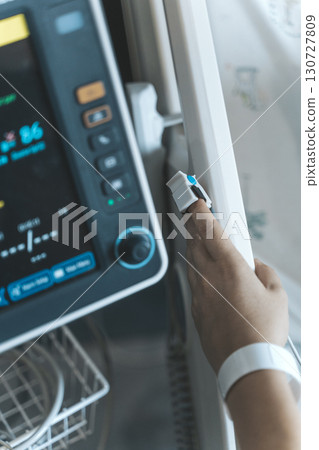 Patient's Finger Connected to Pulse Oximeter on Medical Monitor 130727809