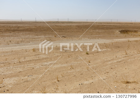 Dry desert landscape with a dirt road and power pylons in Jowzjan Province of Afghanistan 130727996