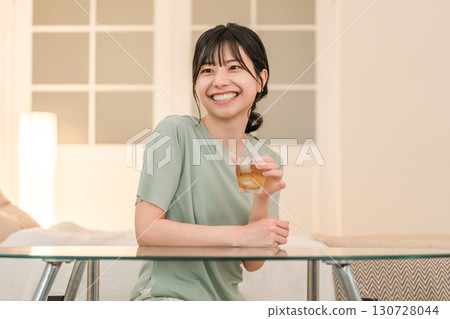 A young Asian woman having a drink in her bedroom at home (drinking at home, tipsy, drinking at home, drinking) 130728044