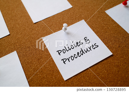 policies and procedures written on sticky note pinned on cork board as reminder 130728895
