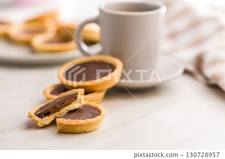 Sweet chocolate tartelettes and coffee cup on white table. 130728957