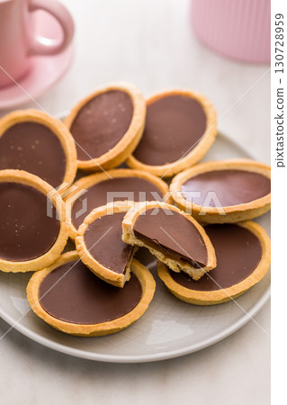 Sweet chocolate tartelettes on plate on white table. 130728959