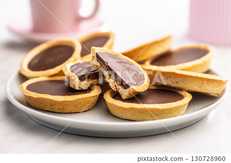 Sweet chocolate tartelettes on plate on white table. Sweet chocolate tartelettes on plate on white table. 130728960